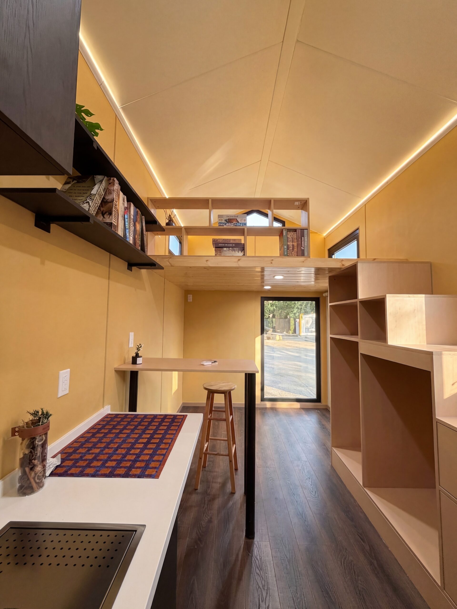 Magic-Nordic 20ft tiny house on wheels interior — kitchen, dining table, and queen loft with built-in bookshelves under gabled roof