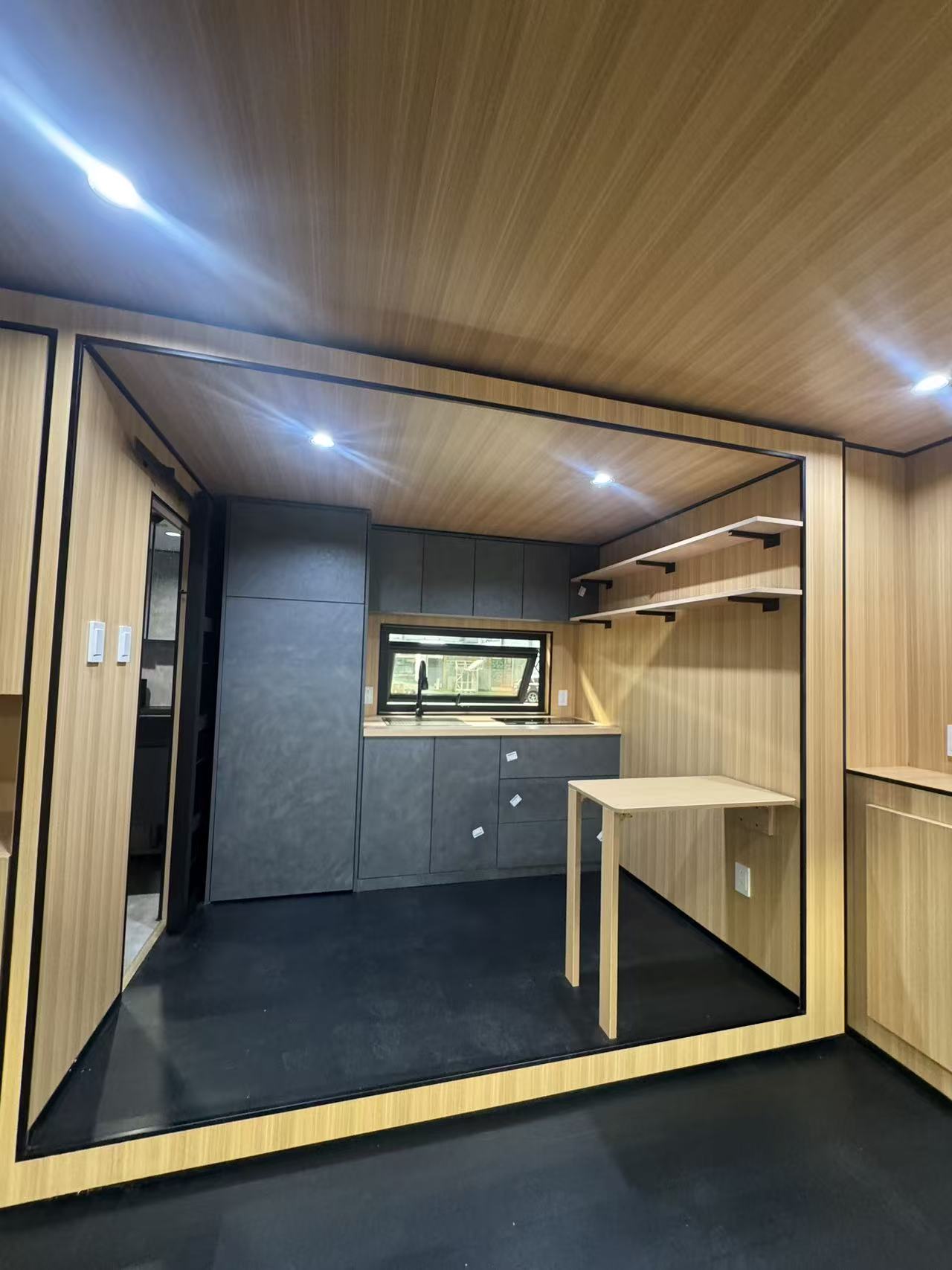 MagicSlide tiny house bathroom with concrete-look walls, black vanity, black toilet and glass shower