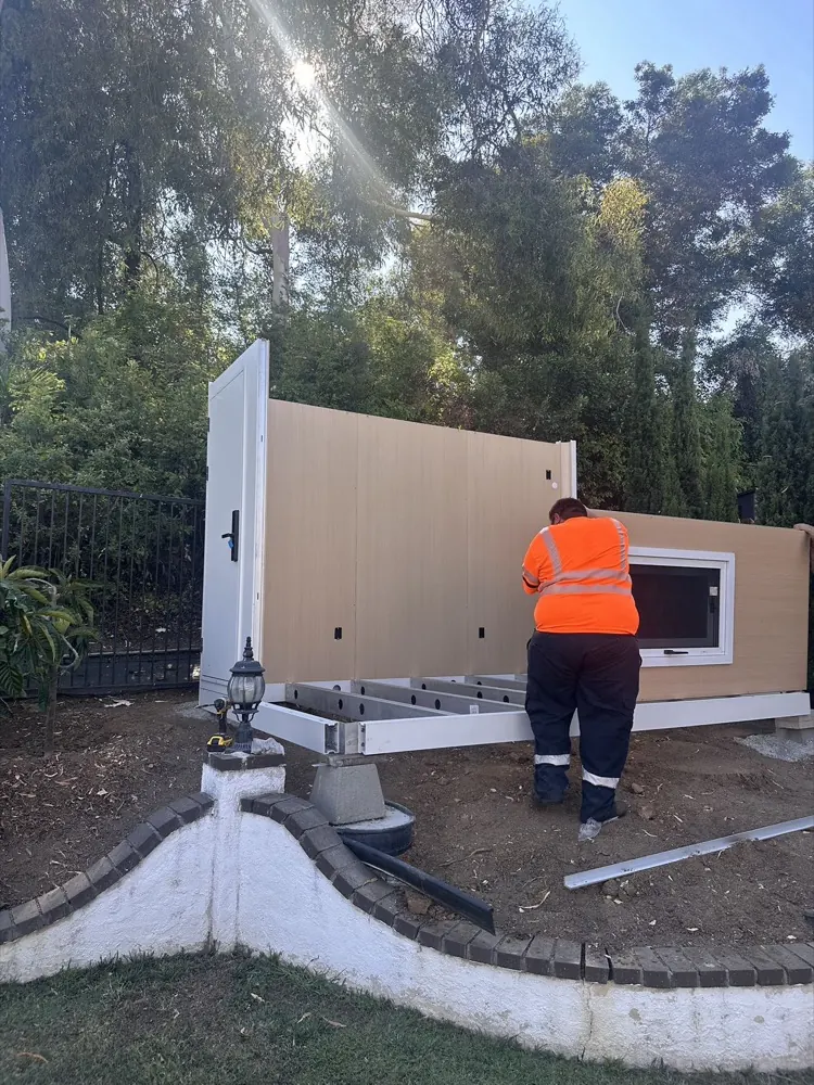 Installer fitting a MagicNest wall panel to the base frame in a backyard